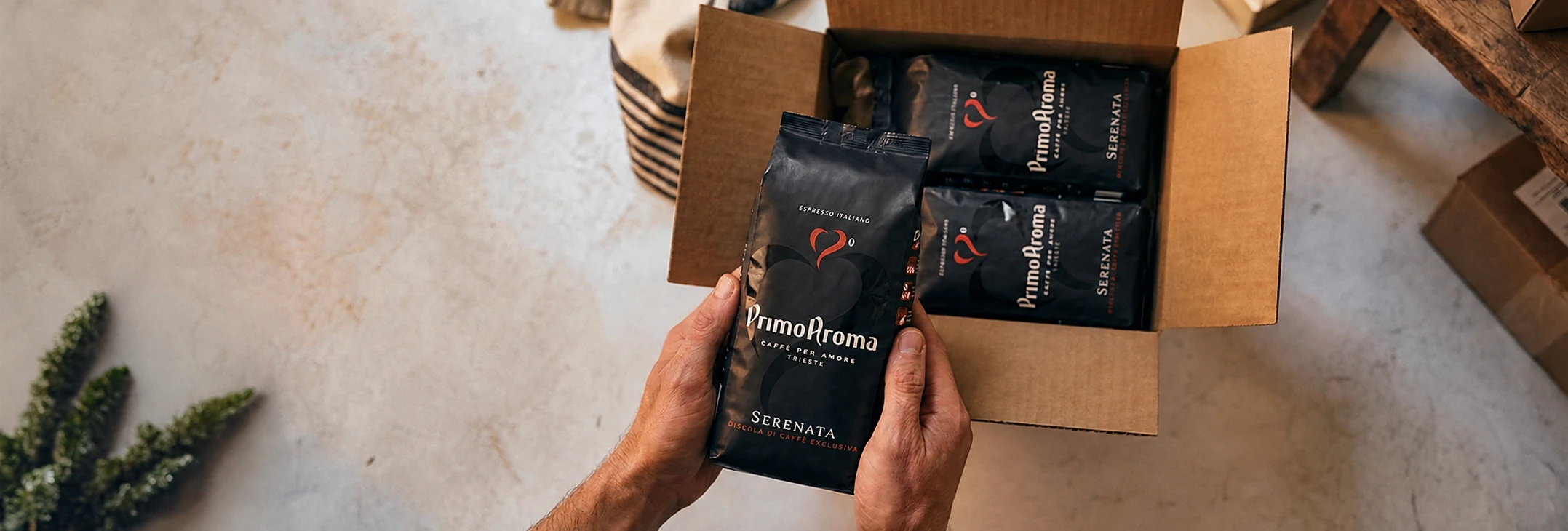 Hände packen eine Primo Aroma Serenata Kaffeepackung aus einem Karton aus